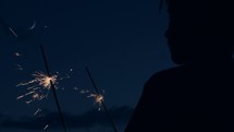 man holding sparklers at night 