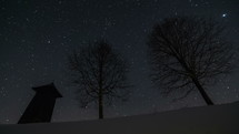 Stars moving in night sky over wooden bell-tower and trees silhouette in winter, astronomy time lapse, dolly shot
