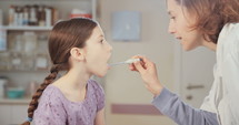 Female doctor checking a young girl's temperature using an oral thermometer in the clinic.