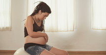 Pregnant woman sitting on a yoga ball holding and rubbing her belly.