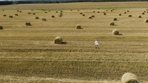 Carefree woman running through golden wheat field. Happy girl in white dress with long developing hair running through field. 