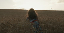 young girl in a golden field during sunset raising her hands in happiness