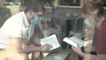 Men wearing face masks reading and discussing scripture in a coffee shop 