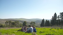 A family with 4 children having a picnic outdoors on a green hill in the sun