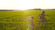 Three happy young kids running together in a green field during sunset