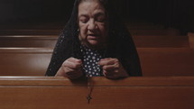 Hispanic woman in a pew in a chapel praying the rosary