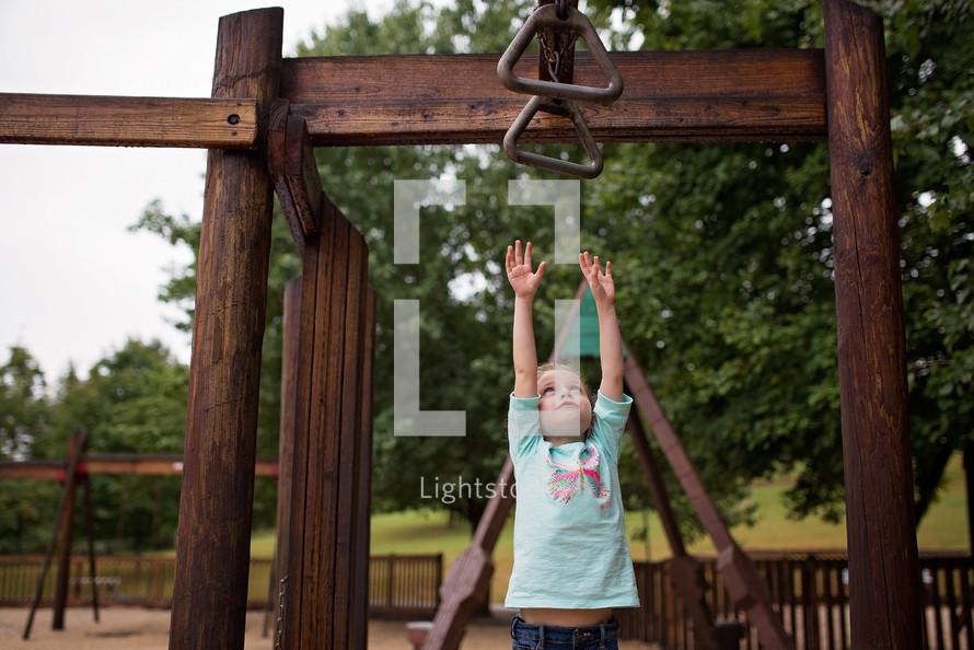 a girl reaching up for monkey bars on a playground 
