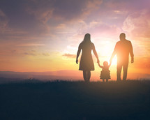 silhouette of a mother and father holding their daughters hand at sunset 