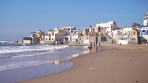 Tourists walk on the sand beach in small Morocco town in Sunny Summer Holiday Vacation in Africa Ocean Coast
