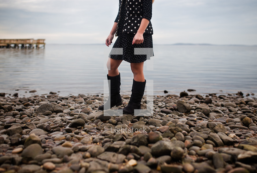 a woman in boots standing on a rocky beach 
