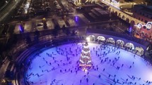 Festive city ice rink with people skating around Christmas tree