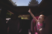 a child in a carseat reaching for a sunroof 