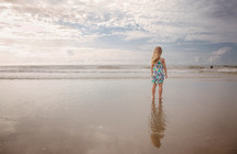 a toddler girl standing in wet sand on a beach 