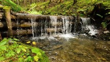Small waterfall cascade in crystal mountain stream in green forest nature background
