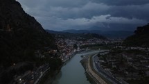 Aerial drone view city of Berat in Albania at dusk, traffic with mountains and clouds in the background