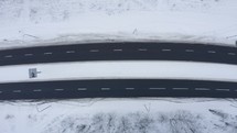Aerial drone view of road in idyllic winter landscape. Top-down aerial view car driving along the road located in the middle of the forest