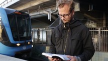 a man standing outdoors at a train station reading a Bible 