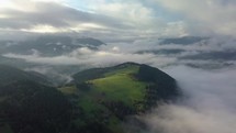 Aerial foggy country landscape in morning light above clouds with beautiful colors at sunrise. Pan left to right
