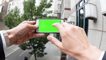 Personal perspective of a businessman holding a smartphone with a green screen - editorial use only
