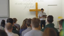 Man preaches or teaches the Bible in a chapel to a group of young adults