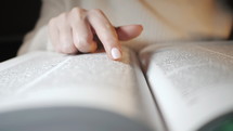 Woman flipping open a Bible, removing the ribbon bookmark, and tracking with her finger.