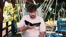 Man sitting in a hammock chair, reading the Bible outdoors