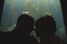 couple kissing in front of a large aquarium 