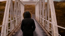 a woman in a coat walking across a covered bridge 