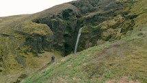 couple watching a waterfall off a green mountainside 