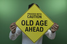 man holding up a Proceed with caution old age ahead sign 