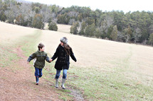 A woman and boy in winter clothes running through a field.
