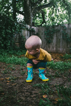 toddler boy in rain boots in a backyard playing in mud 