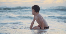 Young boy playing on the beach in the water during sunset hour
