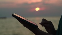 Using touchpad on the beach at sunset