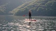 woman riding a paddle board on beautiful lake with tree covered mountain peaks