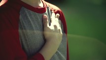 Boy placing his hand over his heart outside.