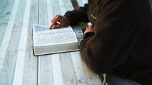 a man sitting at a picnic table reading a Bible 
