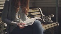 woman reading a Bible sitting on a park bench