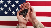 Military Holds Rosary with American flag on background 