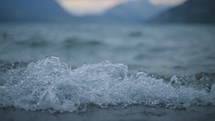 Rack focus of wave and mountains on the shore of a mountain lake in slow motion
