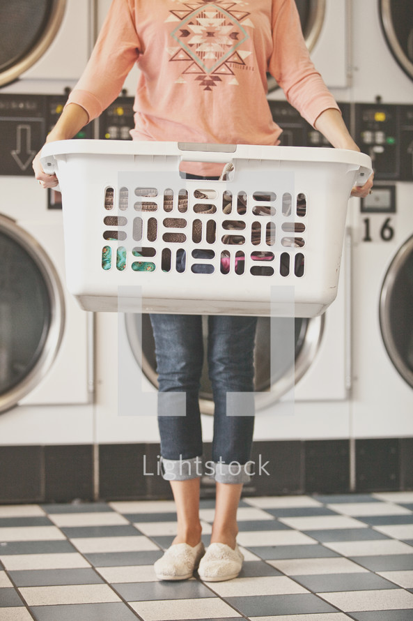 a woman holding a basket full of laundry at a laundromat