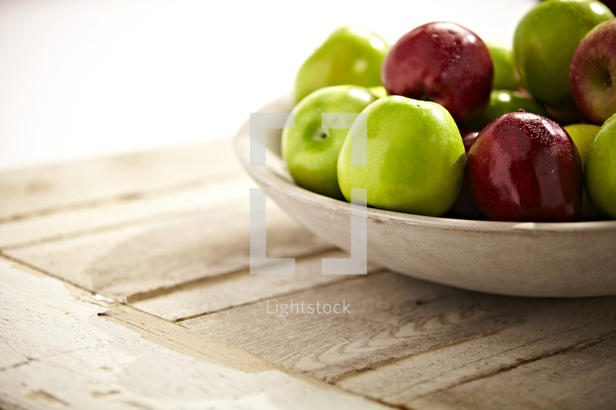 A group of green and red apples sit in a bowl