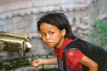 Nepalese girl child washing her hands and drinking from an outdoor spigot [For similar search ethnic smile]