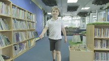a boy walking through the library of a school