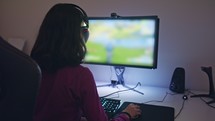 Teenage girl sitting in front of a computer, playing a game wearing a headset