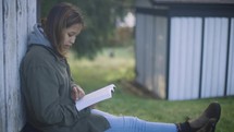 A young woman sits alone reading her Bible outside in a peaceful setting.