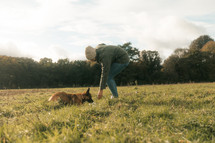 Dog and owner in a field, playing with dog, puppy training, young German Shepherd Alsatian, woman wearing green coat,