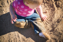 A baby sitting and playing in sand.