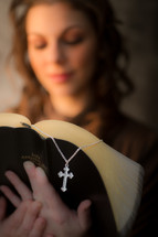a woman reading a Bible and a cross necklace bookmark