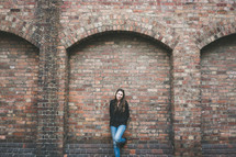 A woman stands against a brick wall with arches.